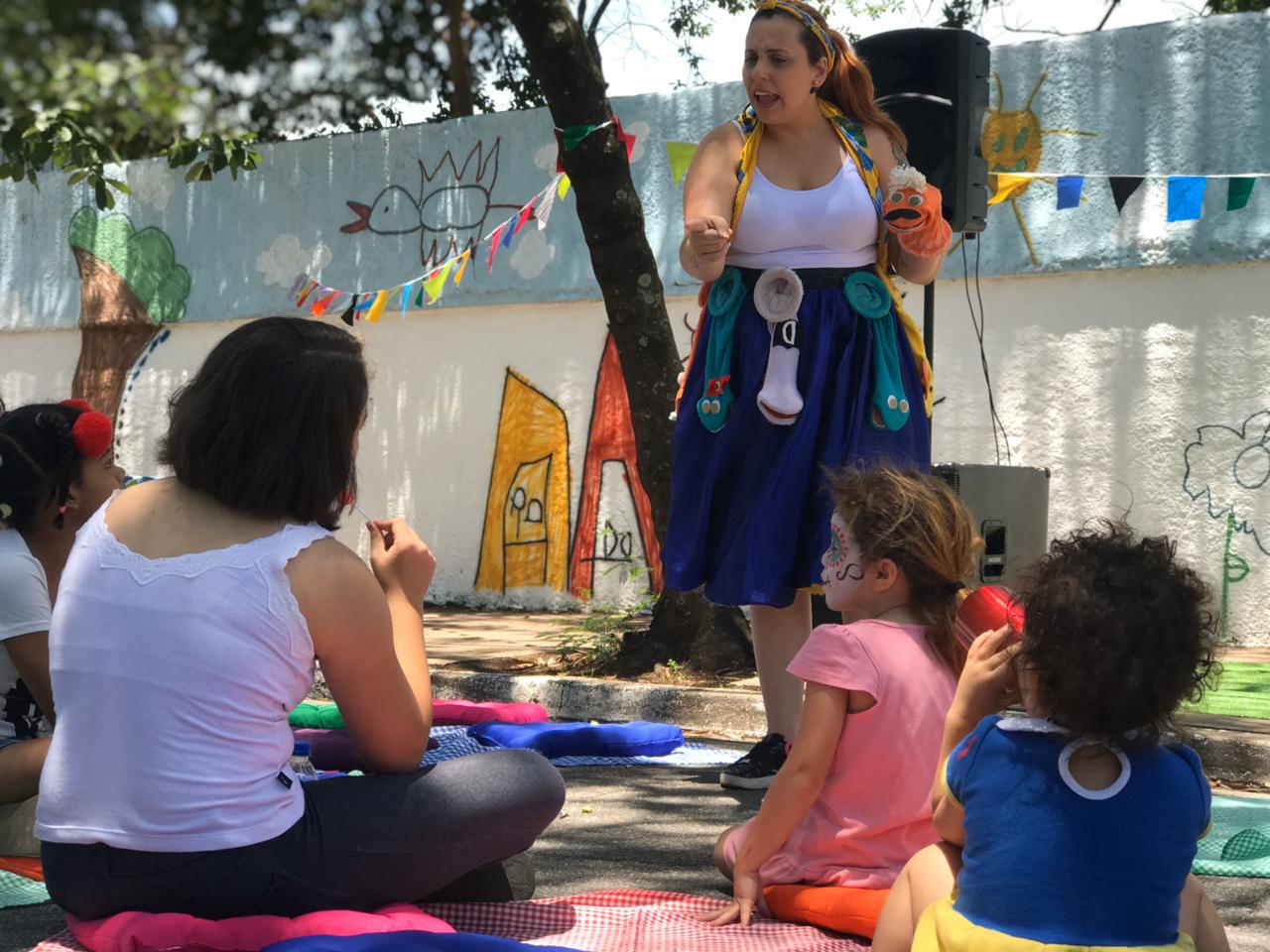 Artista com vestimenta colorida atraia público infantil e adulto sentado entre almofadas